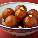 Gulab Jamun: Close-up of golden brown, syrup-soaked Gulab Jamun balls, garnished with chopped nuts, arranged in a traditional serving bowl.